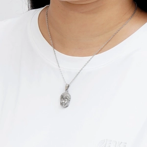 Close-up of a silver buddha head pendant necklace worn by a model on a white background