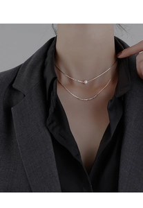 Silver double-layer necklace with white pearl on snake chain worn with a dark suit