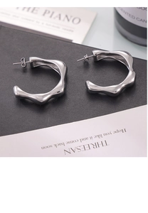 Macro view of silver wave texture earrings with irregular flow lines on a black background