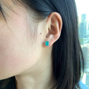 Macro side view of an emerald-cut green gemstone stud earring with four-prong silver setting