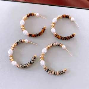 Orecchini a C con pietre occhio di tigre e perle bianche su sfondo grigio elegante