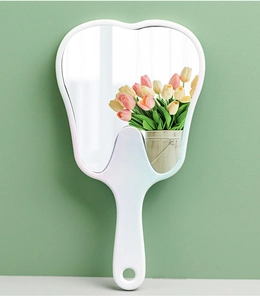 Close-up of a white tooth-shaped handheld mirror reflecting colorful tulip flowers