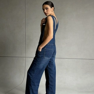 Detailed side view of dark blue denim overalls featuring loose fit and utility pockets