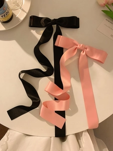 Detailed view of pink and black long ribbon satin hair bows on a white surface