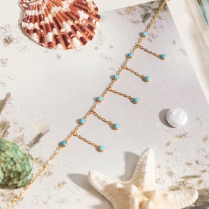 Détail du collier en chaîne dorée avec pendentifs turquoise sur coquillages et perle