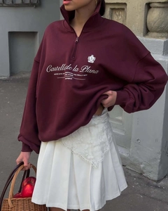 Detail of burgundy half-zip sweatshirt with white pleated skirt and logo embroidery