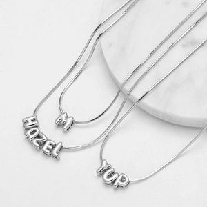 Collana con ciondolo a lettera in argento lucido con catena a serpente su base di marmo