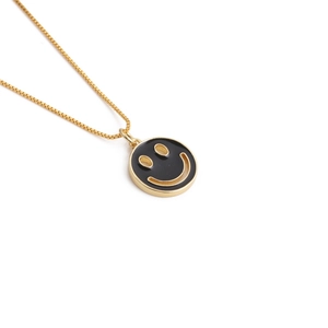 Detail shot of a golden box chain with a round black enamel happy smiley face pendant