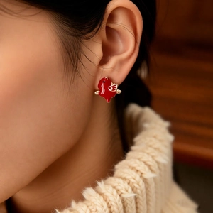 Close-up of a 18k gold plated horse earring with red enamel on a model wearing a beige sweater