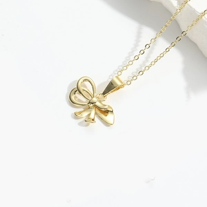 Close-up of golden bow pendant with cross chain on a minimalist white stone background