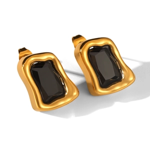 Détail de boucles d'oreilles irrégulières en acier doré et zircons noirs sur fond blanc