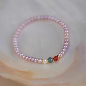 Macro detail of lavender and white pearls with cyan jade and red beads on a gold bracelet