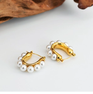 Close-up of gold U-shaped hoop earrings with pearls on a minimalist background
