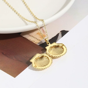 Golden shell locket necklace with minimalist cross chain shown on elegant white tray