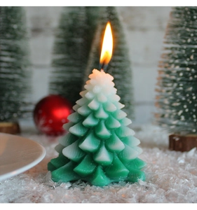 Close-up of a green gradient Christmas tree candle with flame and faux snow texture