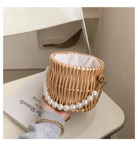 Detail of woven straw bucket bag featuring a large pearl handle and gold chain strap