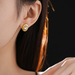 Close-up of gold oval stud earring with central gemstone and small diamonds on ear