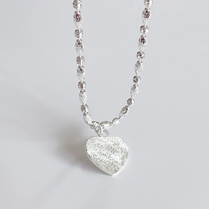 Macro view of textured heart pendant and faceted olive chain in 925 sterling silver