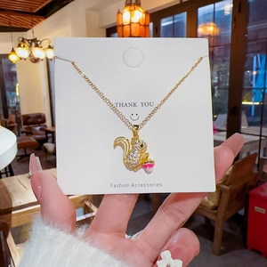 Gold squirrel necklace with zircon inlay holding a pink nut on a white display card