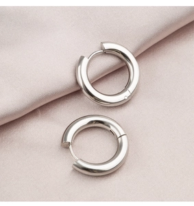 Detailed close-up of thick silver hoop earrings on a soft pink silk background