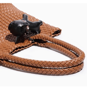 Close-up of brown woven leather handbag with a black French bulldog charm and metal studs