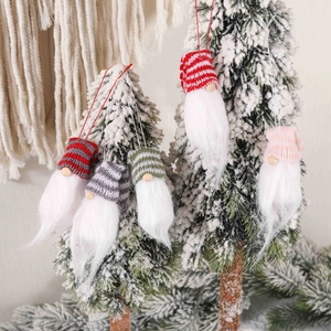 Handmade knitted Christmas gnomes ornaments set hanging on a snow-covered pine tree