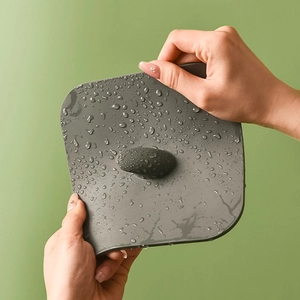 Flexible grey silicone drain cover mat with water droplets on a green background