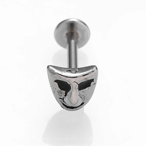 Détail macro d'un piercing en acier 316L avec un motif de masque de théâtre vintage