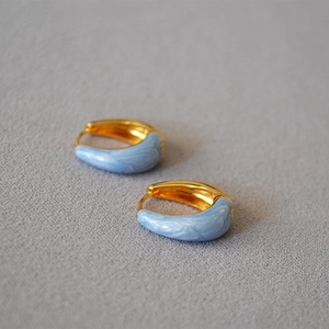 Dettaglio ravvicinato di orecchini a cerchio in ottone dorato con smalto blu marmorizzato