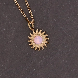 Close-up of golden sunflower pendant with pink gemstone on dark stone background