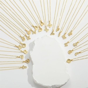 Minimalist gold letter pendant necklaces with hammered texture arranged on white stone
