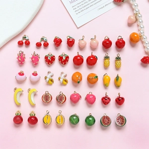 Assorted gold-plated fruit pendants for DIY jewelry making on soft pink background