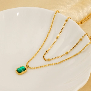 Close-up of gold double-layer titanium necklace featuring a green rectangle gemstone pendant