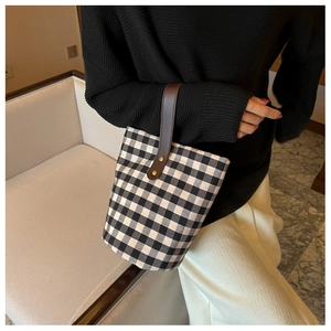 Detail view of a black and white checkered canvas bucket bag with brown leather handles