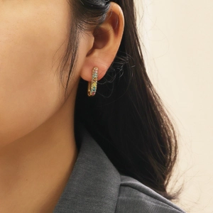 Detail of gold U-shaped hoop earring with rainbow zircon stones on model's ear