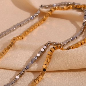 Macro view of gold and silver square beads necklace on soft beige pleated fabric background