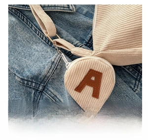 Detail of a beige corduroy mini pouch charm with leather letter A on a tote bag