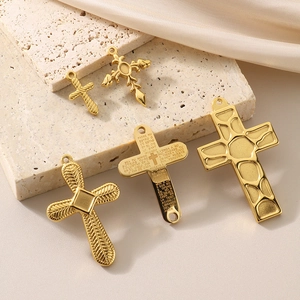 Five gold vintage stainless steel cross pendants displayed on stone and silk background