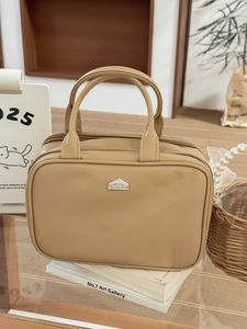 Close-up of beige leather travel toiletry bag with silver triangular logo and dual zippers
