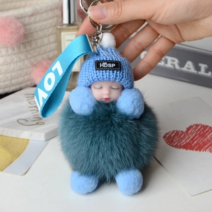 Close-up of fluffy fox fur ball keychain with sleeping baby doll and blue knitted hat