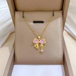 Dettaglio della collana in titanio dorato con fiocco in zircone rosa e quadrifoglio viola