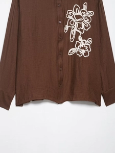 Detail of white flower embroidery on brown long-sleeve shirt with cotton linen texture