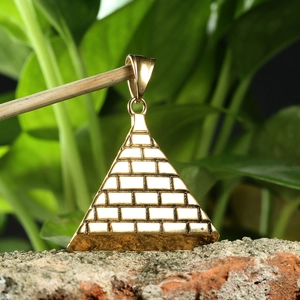 Ancient Egyptian pyramid necklace pendant in gold finish hanging above red brick stones