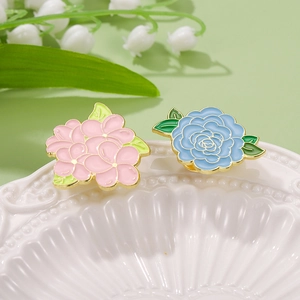 Elegant gold-edged flower enamel brooches in pink and blue on a white ceramic dish