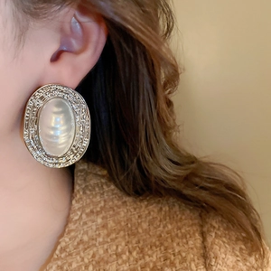 Close-up of a vintage golden oval earring with pearl inlay worn by a model
