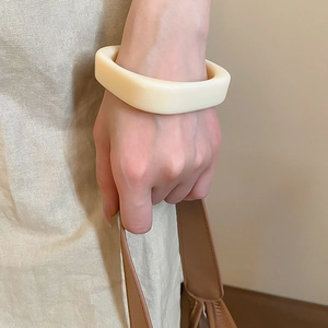 Nahaufnahme eines minimalistischen cremeweißen Harz-Armreifs im quadratischen Design
