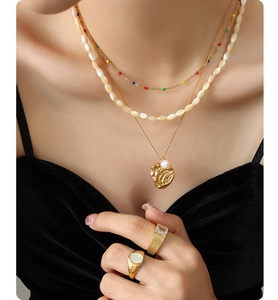 Close-up of layered gold necklaces with freshwater pearls and textured statement rings