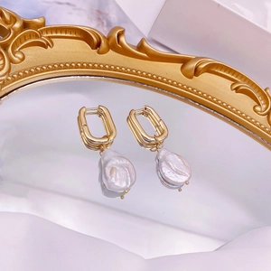 Detailed close-up of Baroque pearl earrings on a gold-rimmed mirror with elegant reflections