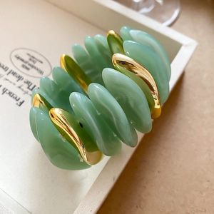 Macro shot of mint green acrylic leaf beads and golden metal components on elastic bracelet
