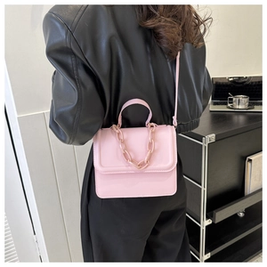 Pink crossbody square bag with chain detail shown on model in a stylish indoor setting